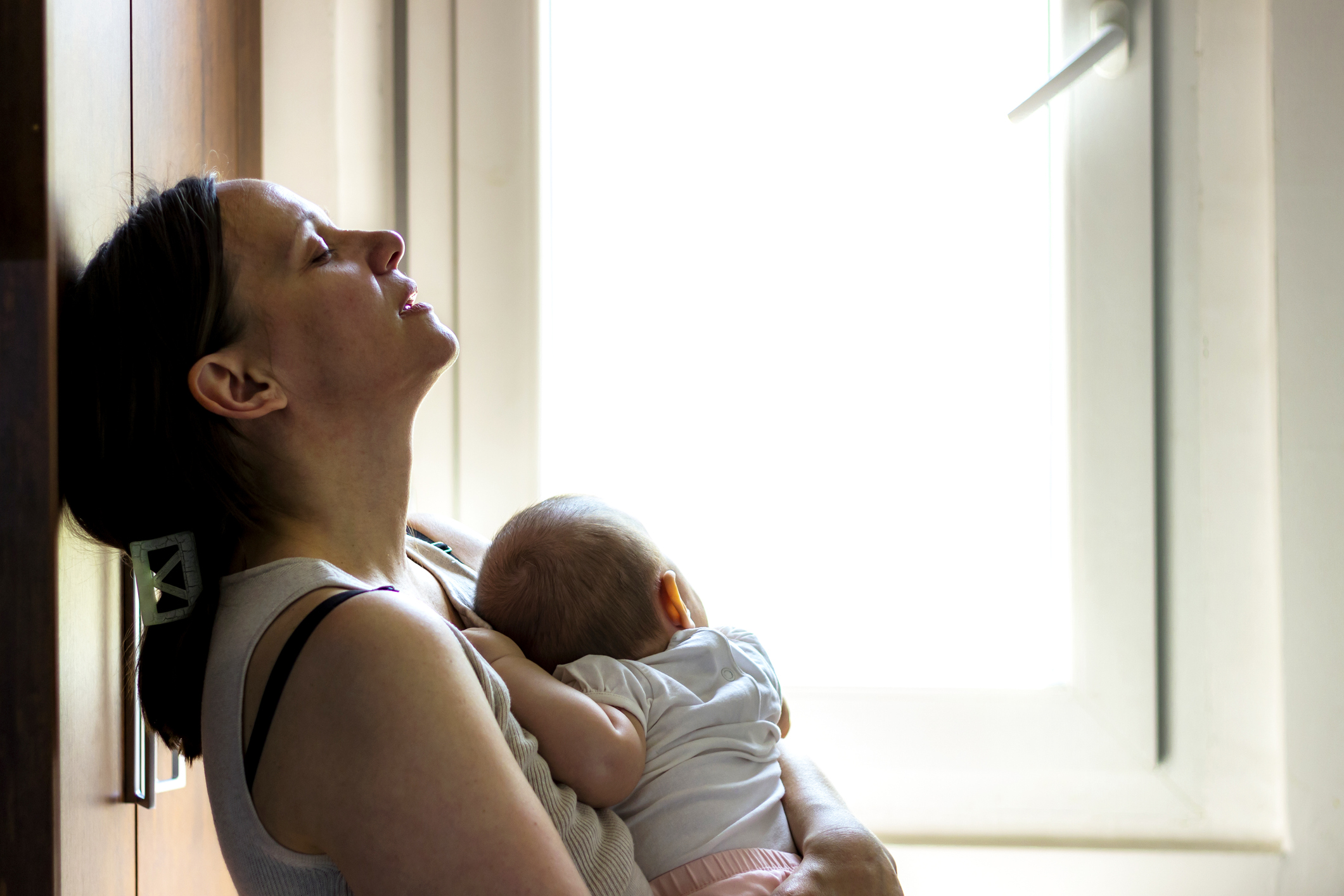 Mom resting against a wall with infant sleeping on her chest