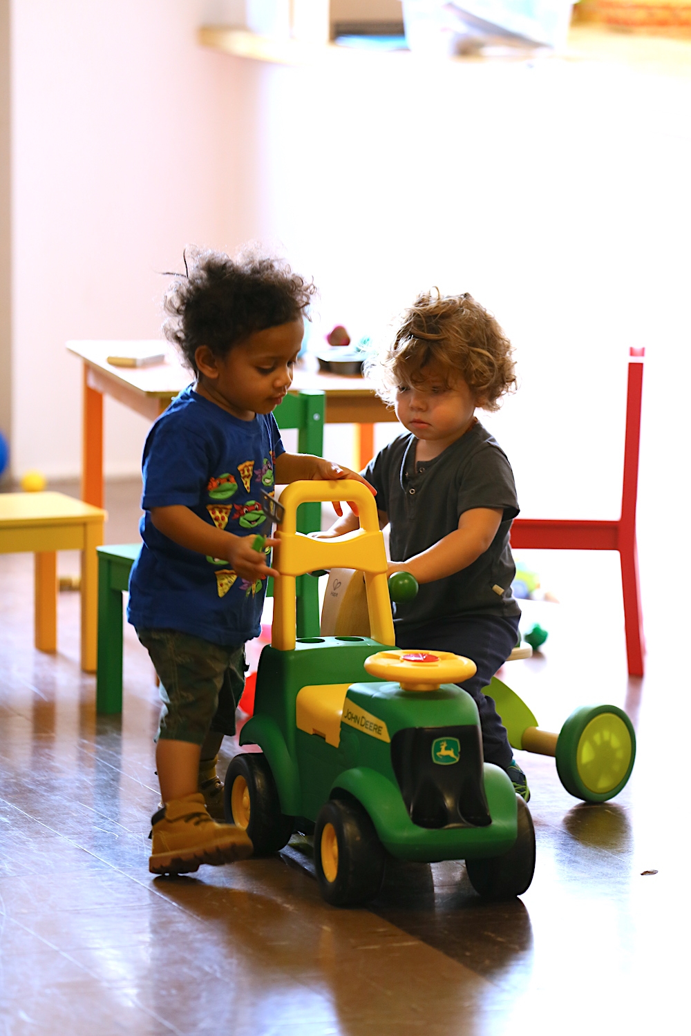 Two toddlers playing with a toy riding tractor