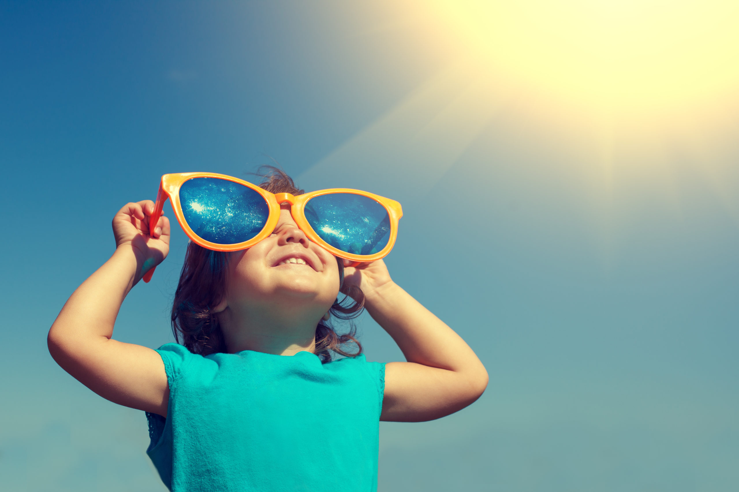 Smiling child with big sunglasses looking at the sun