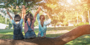 3 preschool children on log outside holding hands with arms raised