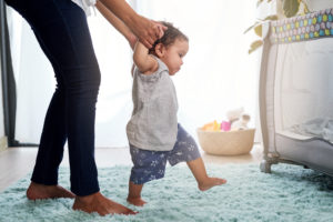 adult holding baby's hands while the baby takes steps