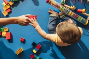 Adult handing a duplo to a baby; view from above