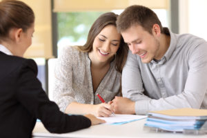 smiling couple filling out paperwork while a 3rd person looks on
